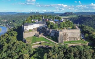 Het fort Königsburg steekt uit tussen de groene bomen. De foto is vanuit vogelperspectief genomen; achter het fort is de stad Königsburg te zien en links stroomt de Elbe.