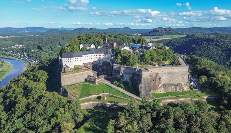 Het fort Königsburg steekt uit tussen de groene bomen. De foto is vanuit vogelperspectief genomen; achter het fort is de stad Königsburg te zien en links stroomt de Elbe.