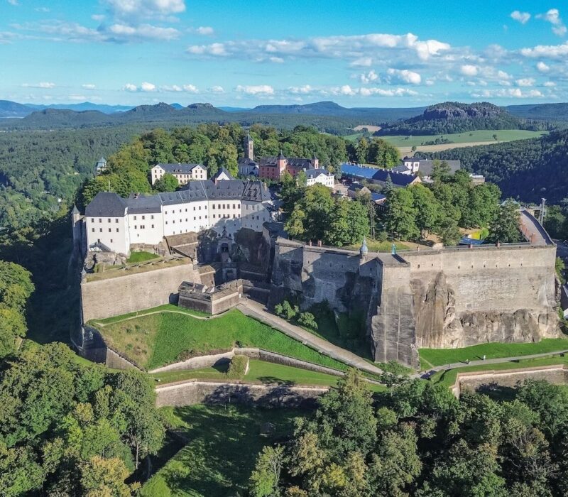 Het fort Königsburg steekt uit tussen de groene bomen. De foto is vanuit vogelperspectief genomen; achter het fort is de stad Königsburg te zien en links stroomt de Elbe.