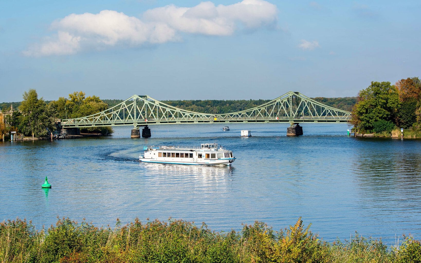 De Glienicker Brücke over de Havel tussen Potsdam en Berlijn, met daarvoor een witte excursieboot van de Weisse Flotte op het water onder een blauwe hemel.