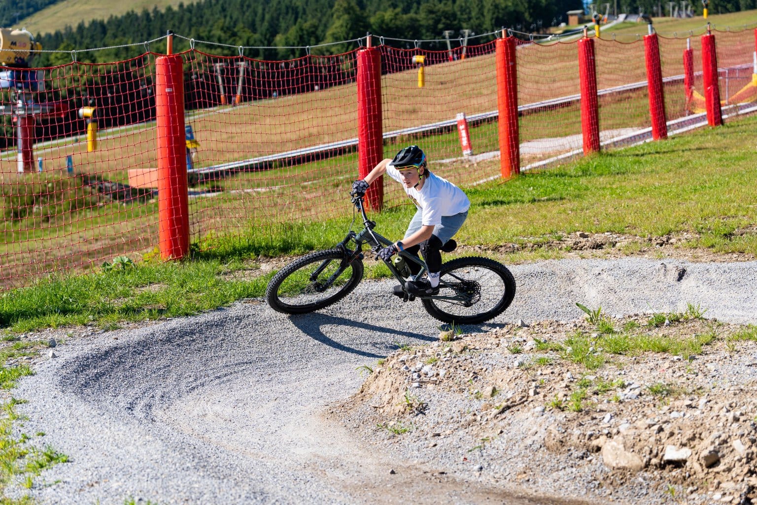 Een kind met een fietshelm rijdt op een mountainbike door een schuine bocht in een bikepark.