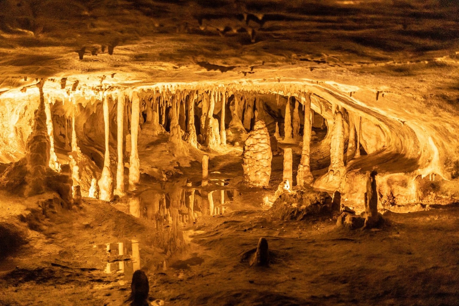 Stalactieten hangen aan het plafond van de Hermanns-grot in Rübenland in het Harzgebergte en worden weerspiegeld in een grotmeer, verlicht door warm oranje licht.