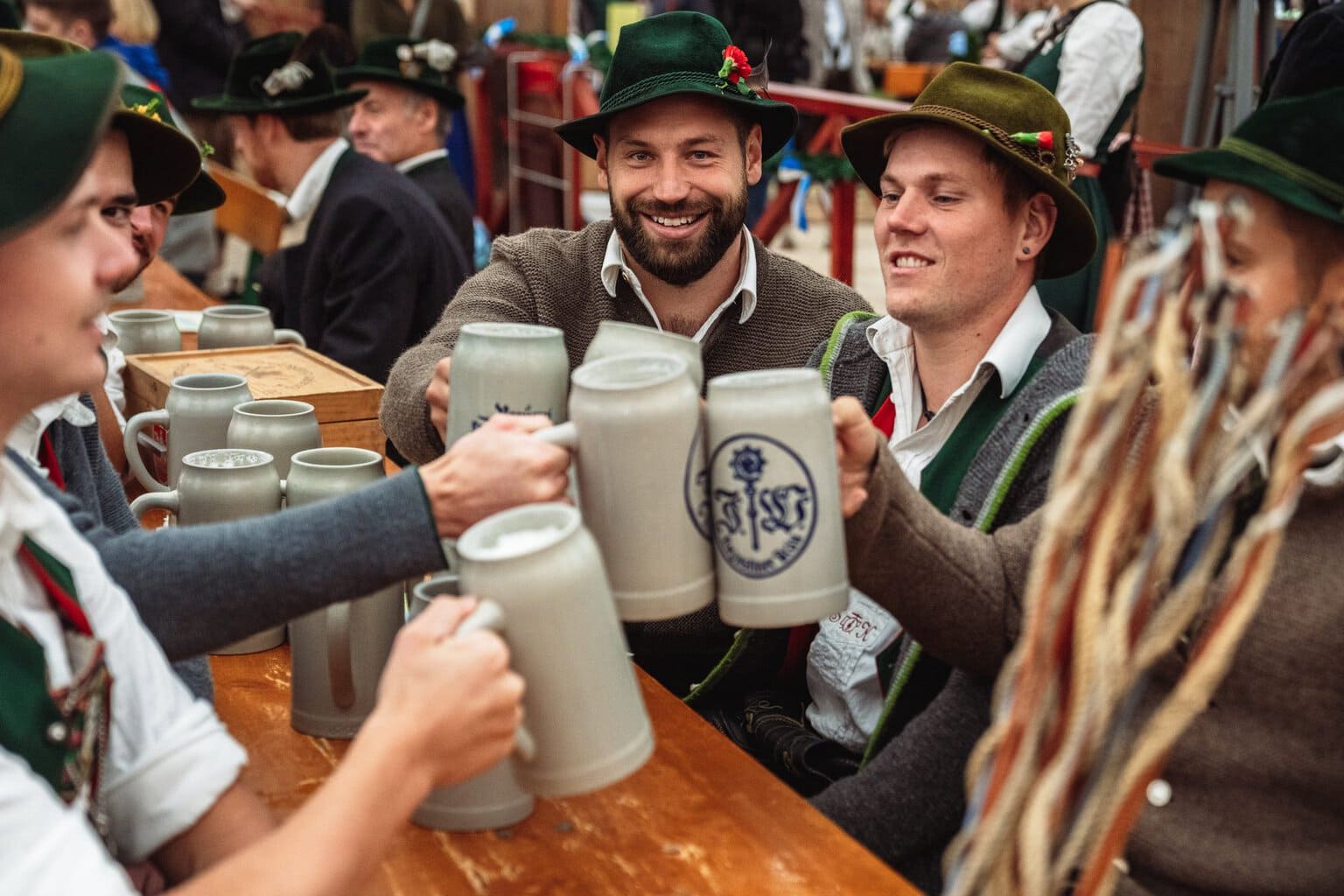 Mannen met groene hoeden en klederdracht proosten met stenen bierpullen in een tent op het Oktoberfest