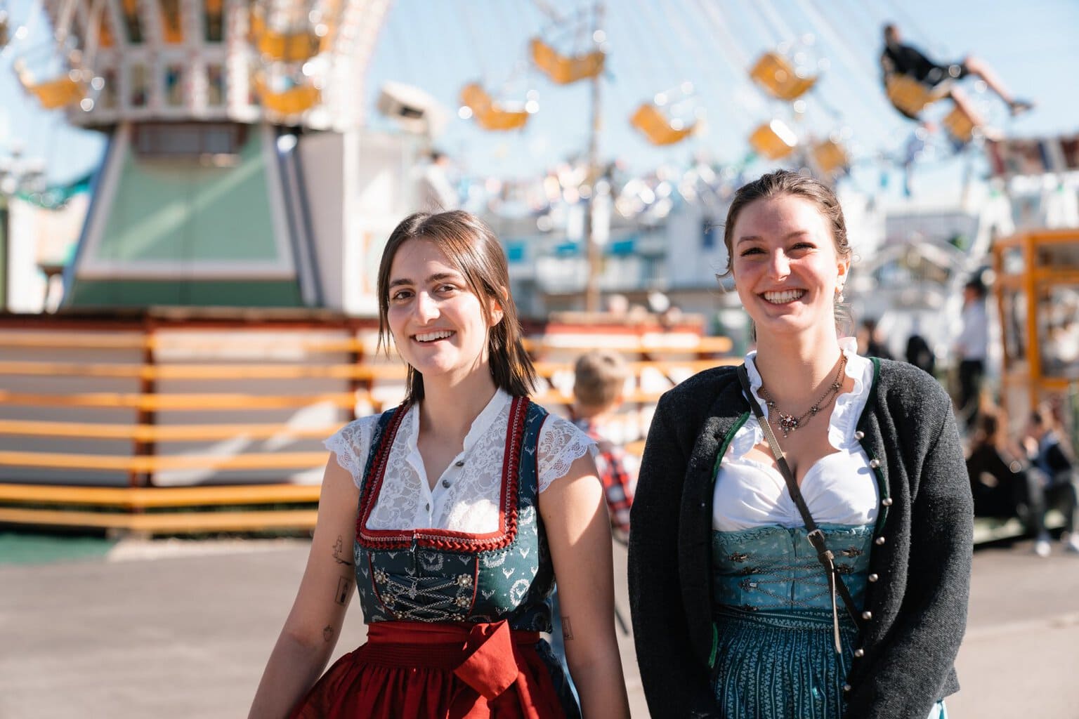Twee lachende vrouwen in dirndl voor een zweefmolen op het Oktoberfest in München