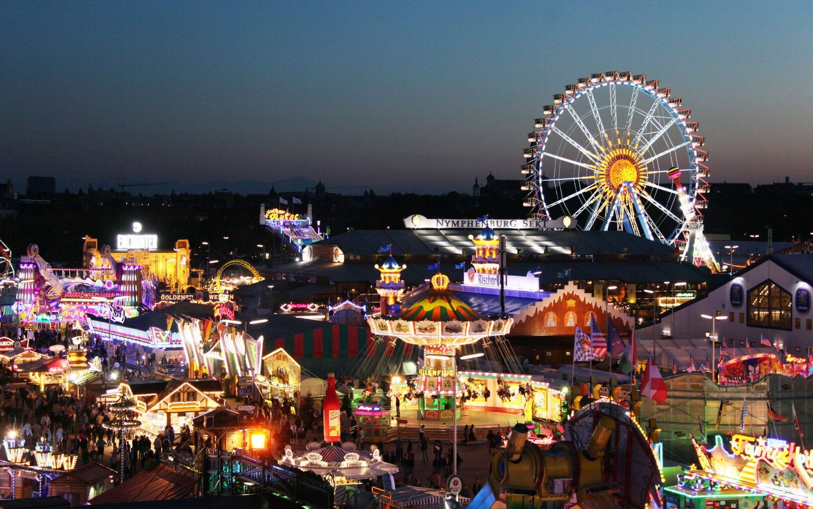 Verlichte attracties en het reuzenrad op de Theresienwiese tijdens het Oktoberfest in de avondschemering