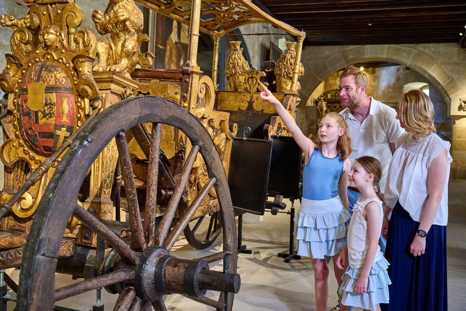 Gezin met twee dochters bewondert een vergulde pronkkoets in het museum van de Veste Coburg, een cultureel uitje met kinderen in Beieren