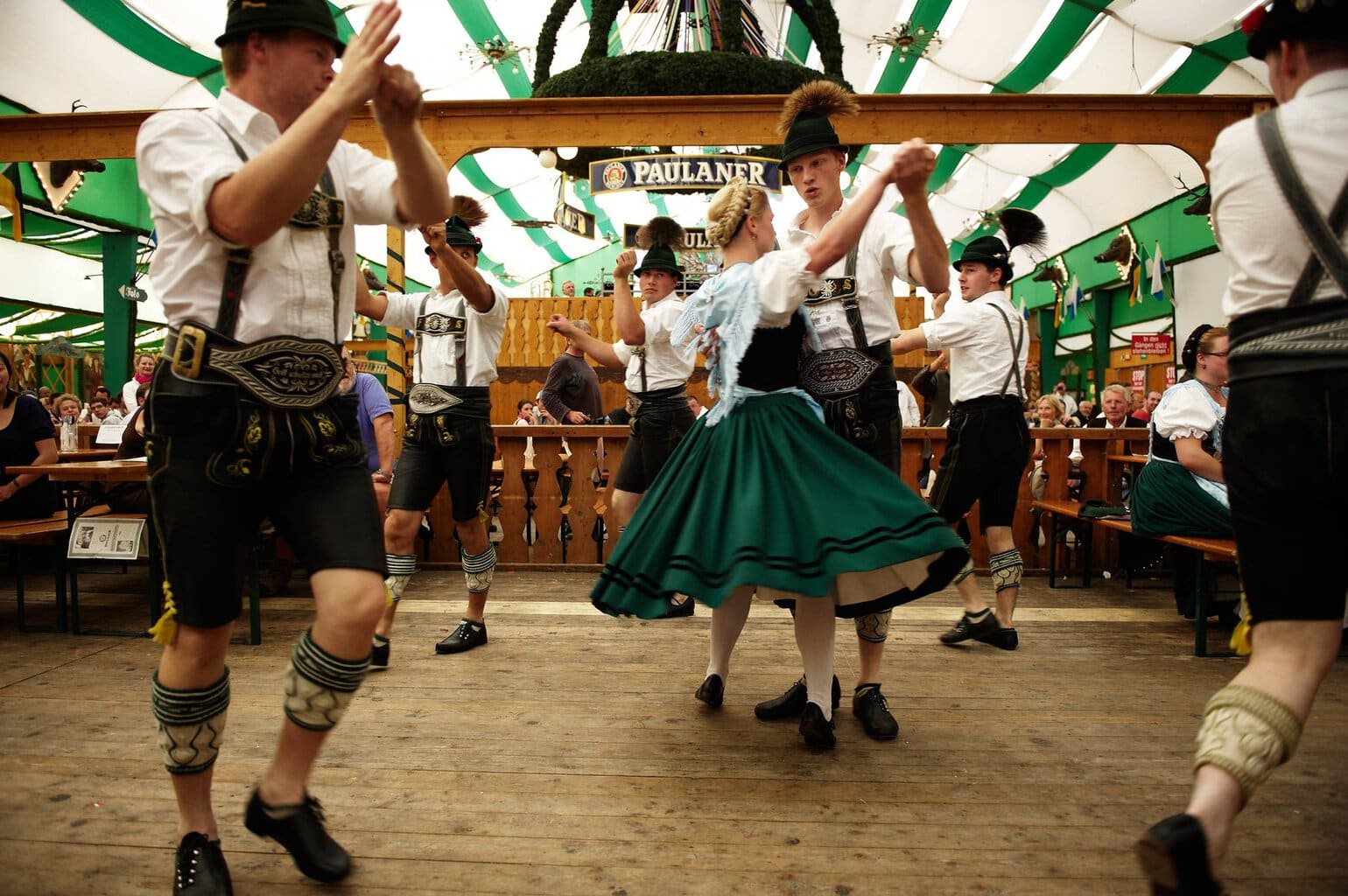 Dansers in lederhosen en dirndl voeren een traditionele Beierse volksdans uit in een feesttent op de Oide Wiesn van het Oktoberfest