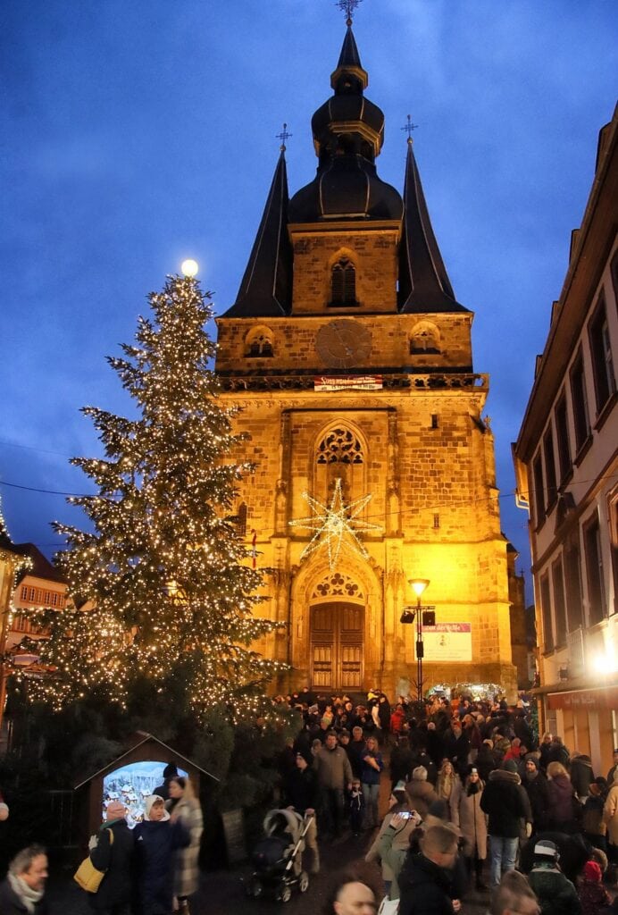 Verlichte basiliek en grote kerstboom met bezoekers op de kerstmarkt van St. Wendel bij schemering